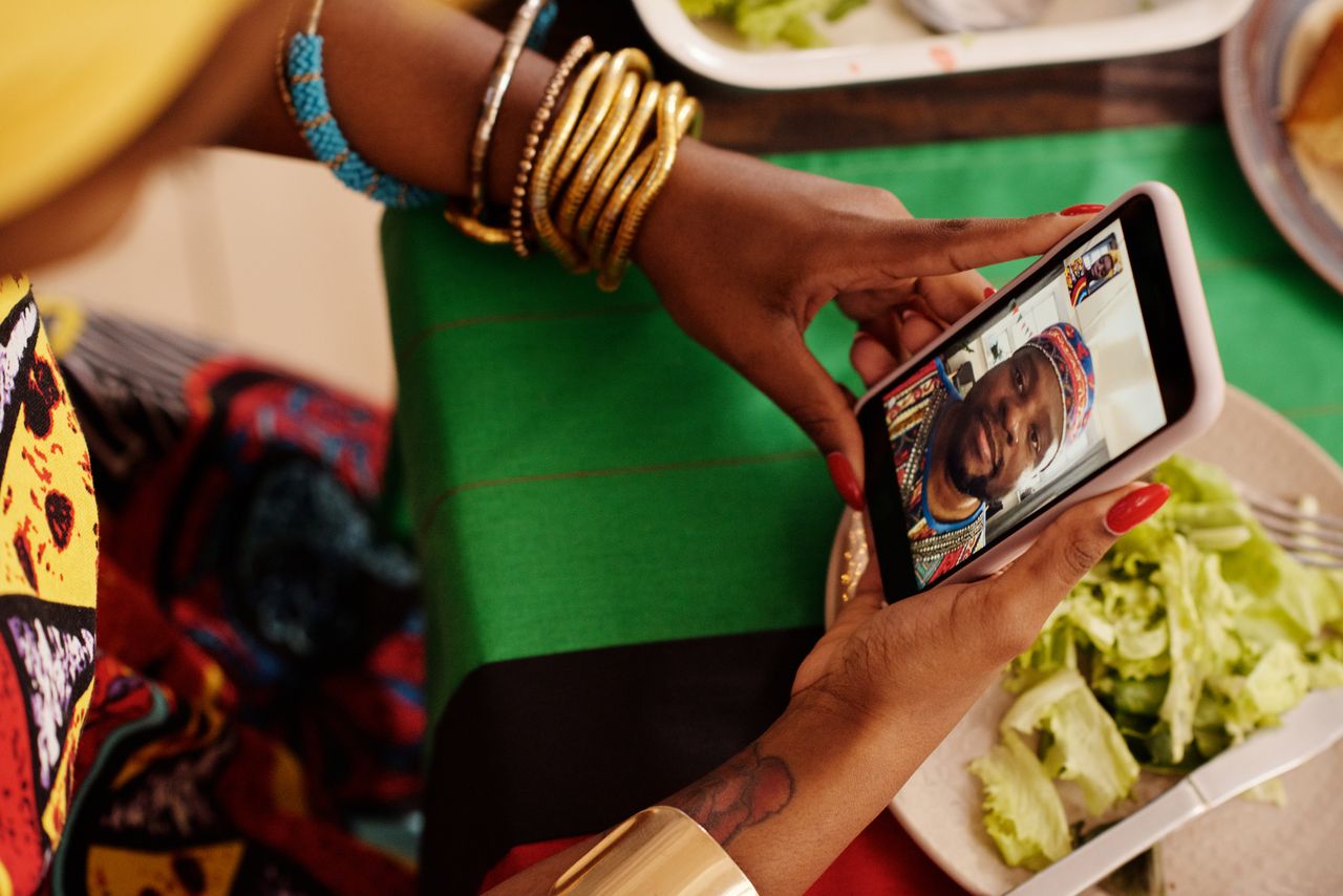 Femme utilisant un smartphone pour un appel vidéo avec un décor de table festif. Célébrer les traditions culturelles en numérique.